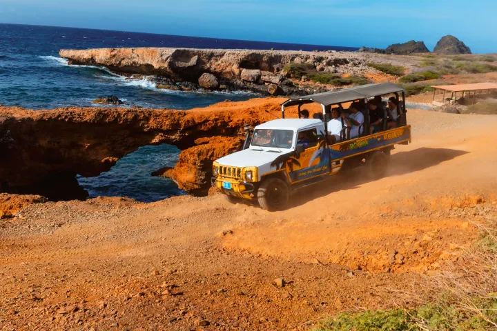 Tour jeep driving on rocky coastal terrain near natural arch and ocean.