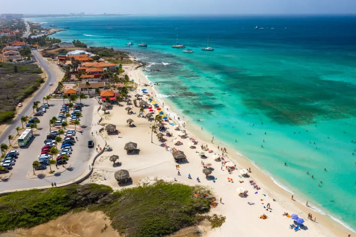Aerial view of a sandy beach with colorful umbrellas and people swimming in turquoise sea.