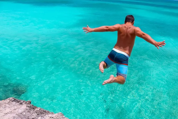 Person jumping off a rock into clear turquoise water.