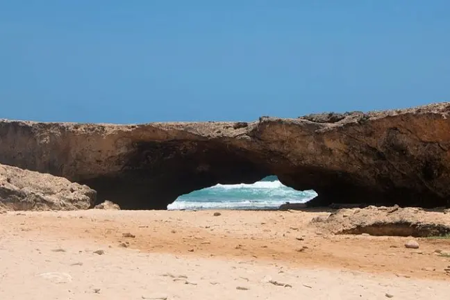 Rocky arch on a sandy beach with ocean waves visible through the opening.