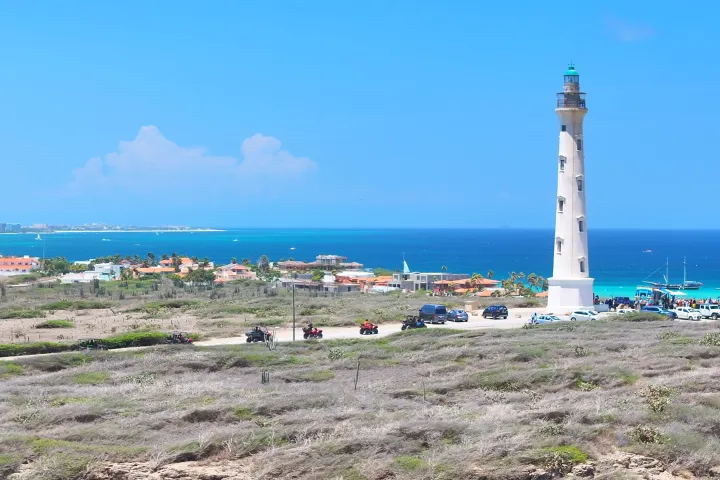 Tall white lighthouse near the coast with ocean and blue sky in the background.