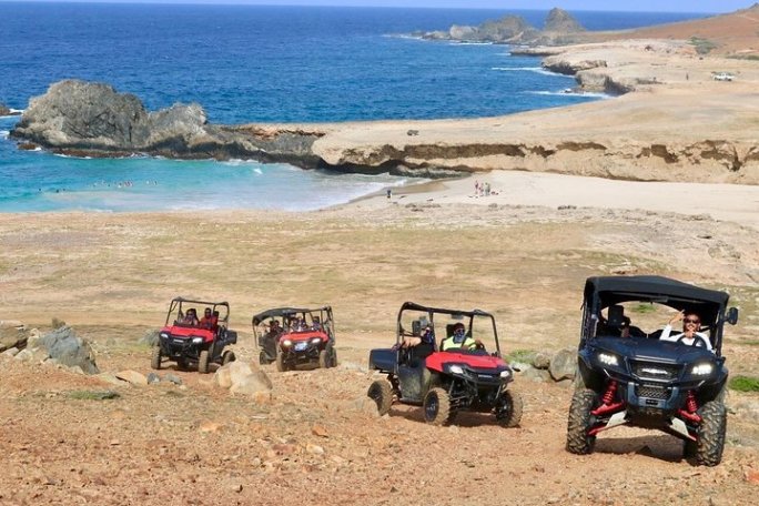 ATVs driving on a rocky coastal trail with ocean and cliffs in the background.