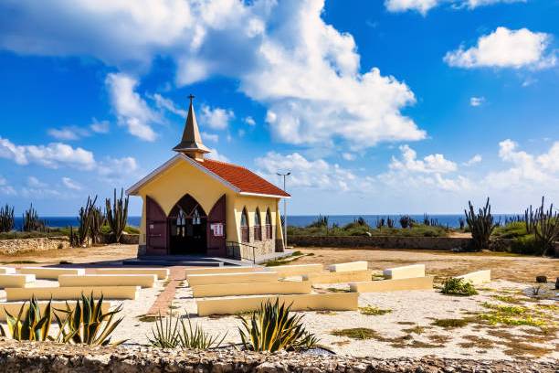 Small chapel with a red roof, surrounded by benches and desert plants under a blue sky with clouds.