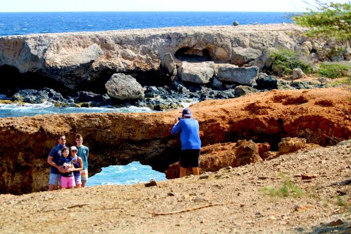 Person photographing a group by a rocky coastline with the ocean in the background.