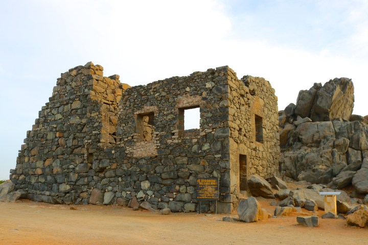 Stone ruins of a building on a sandy landscape with scattered rocks.